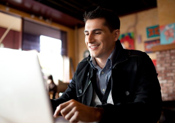 Man sitting in restaurant smiling and looking down at laptop