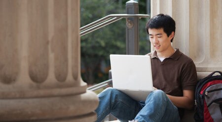 Student sitting on ground against column working on laptop