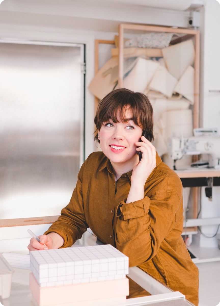 A woman in a brown shirt at a desk on her cell phone taking notes